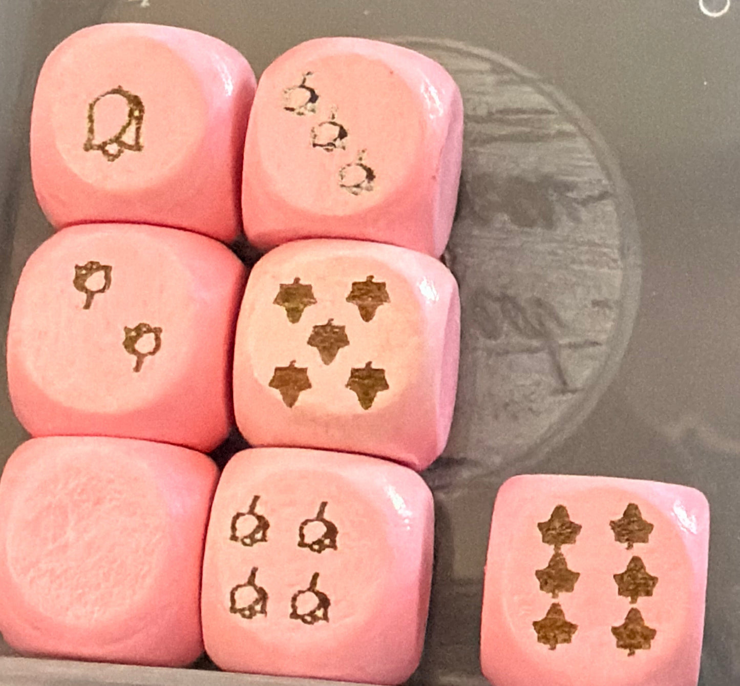 Set of pink dice with symbols in a clear container on a dark surface
