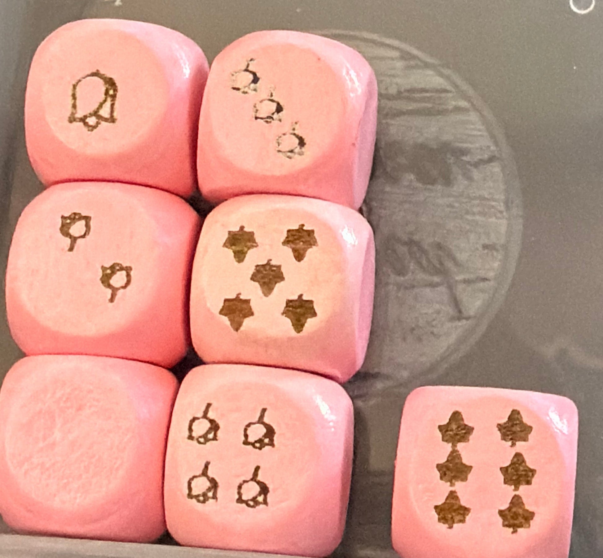 Set of pink dice with symbols in a clear container on a dark surface