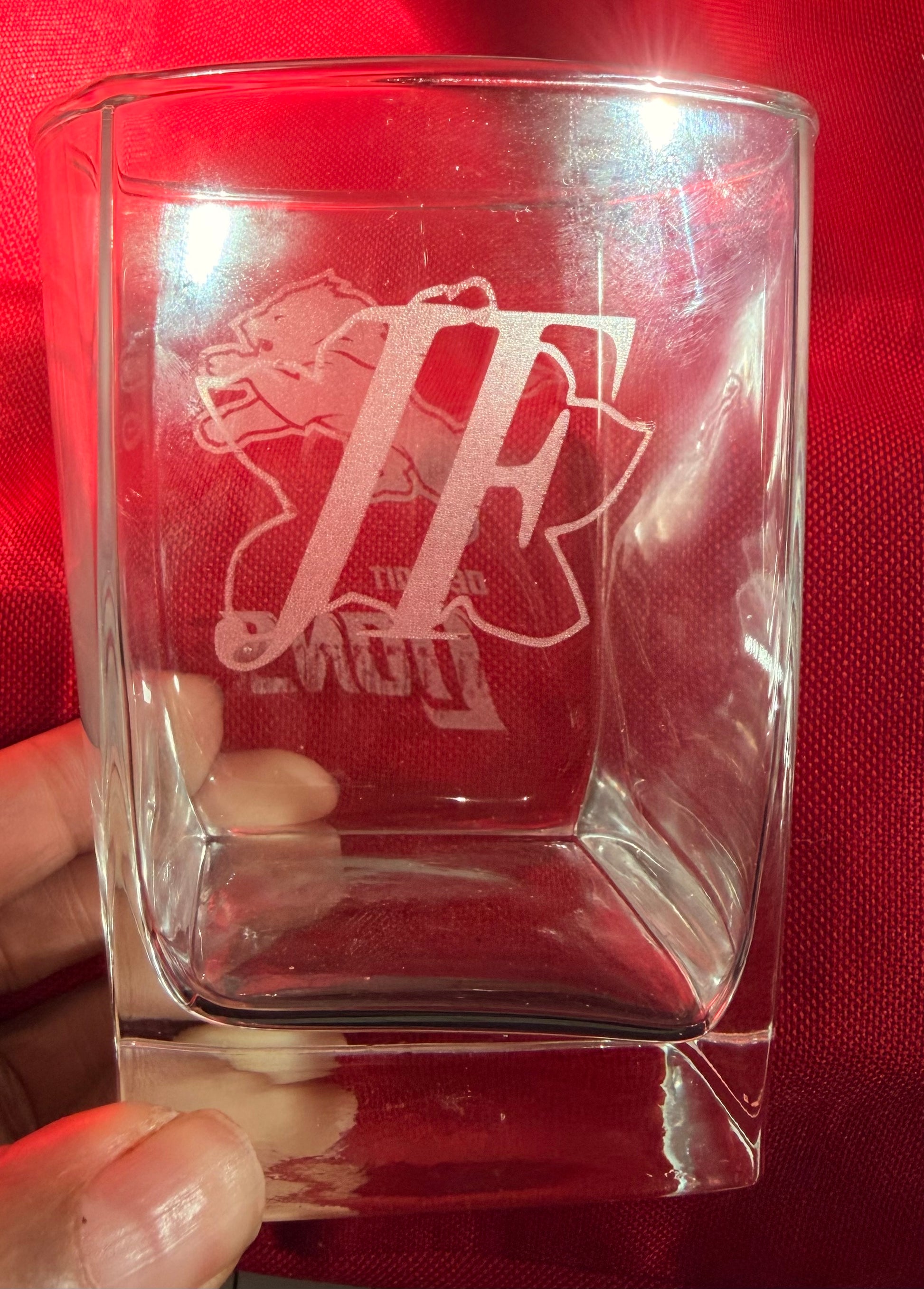 Clear glass with engraved logo held against a red background